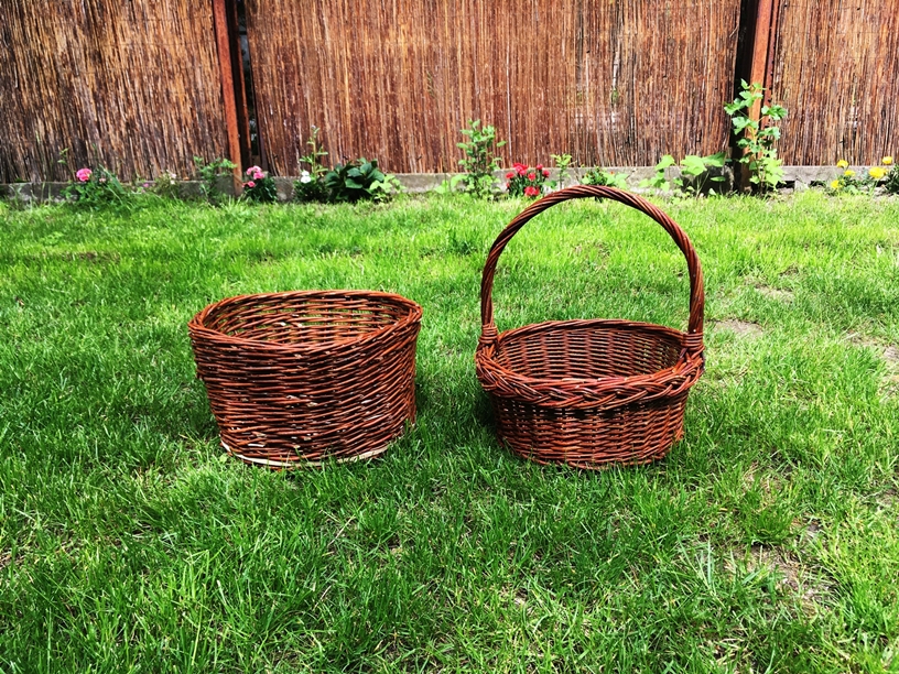 Dwa wiklinowe koszyki, jeden z rączką, drugi bez, postawione na zielonej trawie.