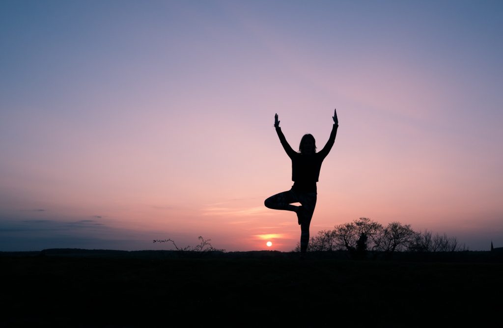 Kobieta uprawiająca jogę na tle zachodzącego słońca.