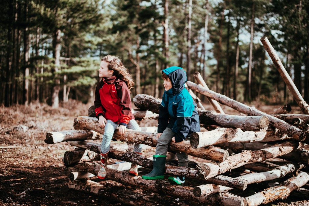 Chłopiec i dziewczynka siedzący w lesie na poukładanych balach drewnianych.