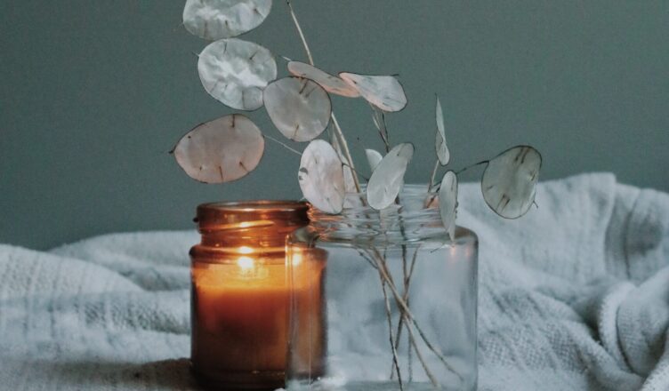 Paląca się świeca w słoiku z brązowego szkła oraz wazon z gałązkami lunarii.