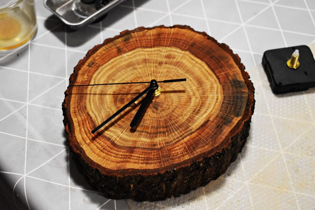 Zegar wykonany z okrągłego plastra drewna z czarnymi wskazówkami.