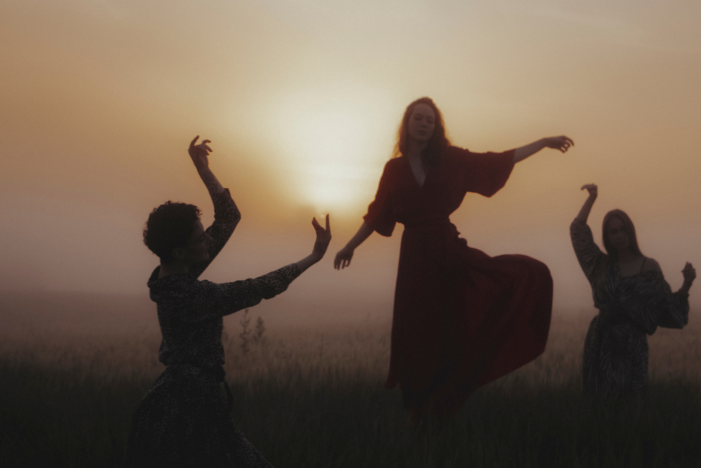 Trzy kobiety tańczą na tle zachodzącego słońca.