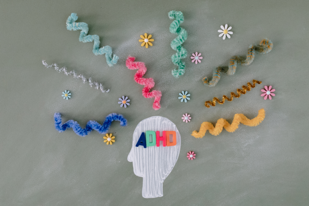 Narysowana głowa z napisem ADHD ze sprężynkami i kwiatkami w różnych kolorach na poziomie głowy.