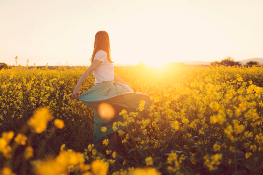 Osoba tańczy na łące żółtych kwiatów o zachodzie słońca.