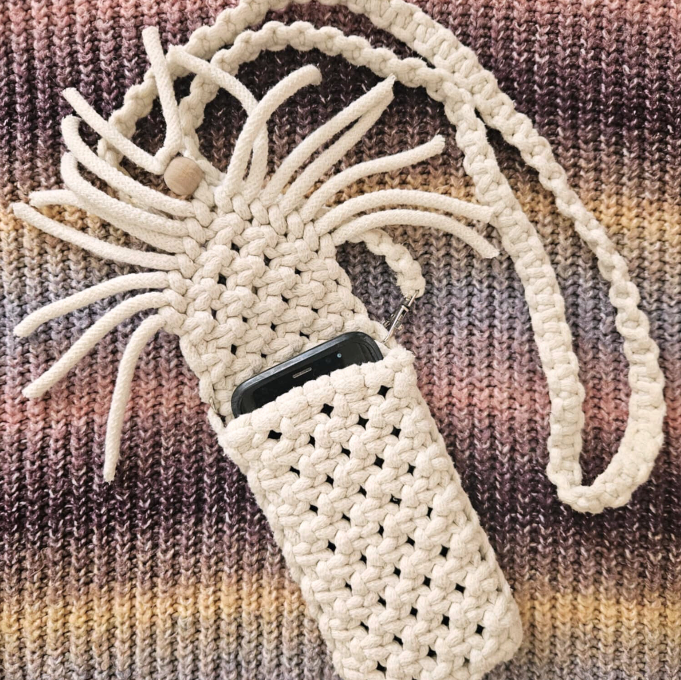 Torebka na telefon wykonana z białej włóczki na tle kolorowego swetra.