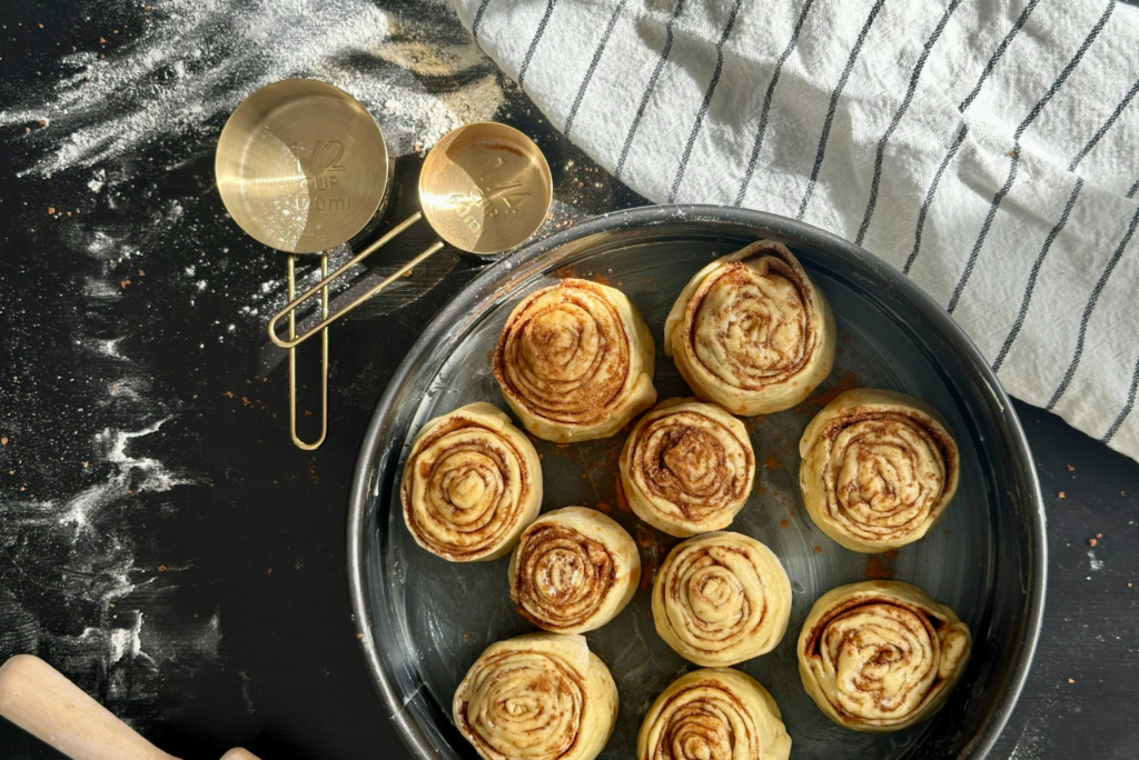 Zawinięte ciasto na cynamonki w blasze do pieczenia na kuchennym blacie.