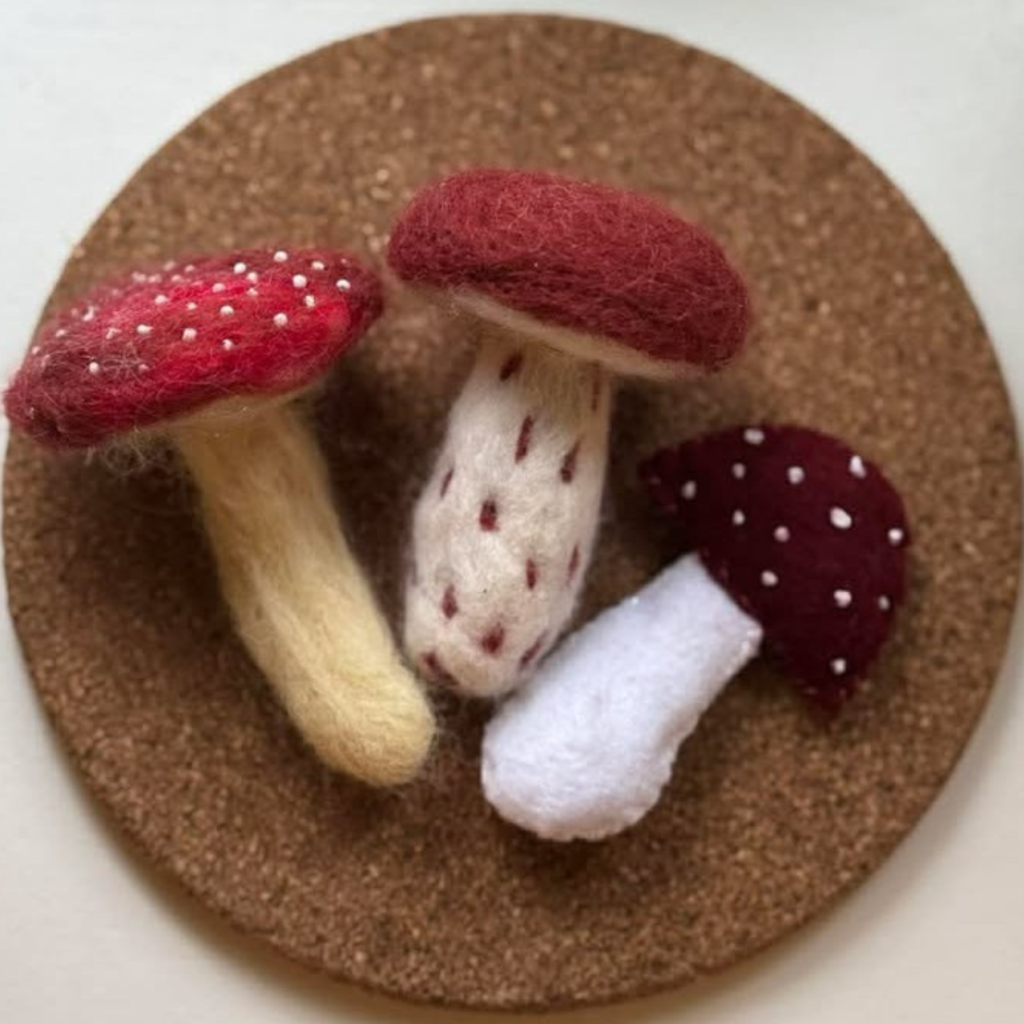 Trzy grzybki wykonane z filcu na korkowej podstawce.
