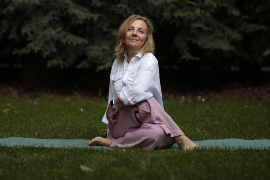 Kobieta siedząca w jogowej pozie na macie w ogrodzie.